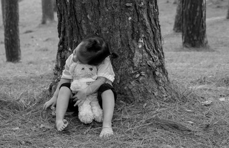 亚洲小女孩正在抱抱熊 独自坐在松树下的地上 笑声学习赤脚探索孤独公园木头教育女性情感拥抱背景