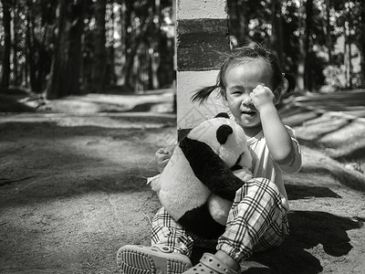 亚洲小孩独自坐在松树林的路上哭泣和抱抱熊时 坐着背景