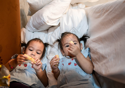 和妹妹一起吃零食的亚洲小女孩 在Thn床房里童年高清图片素材