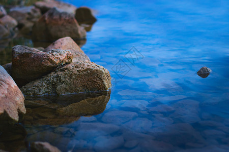 黄昏时湖岸上的自然石块岩石涟漪淡水空间石头环境支撑反射风景蓝色背景图片