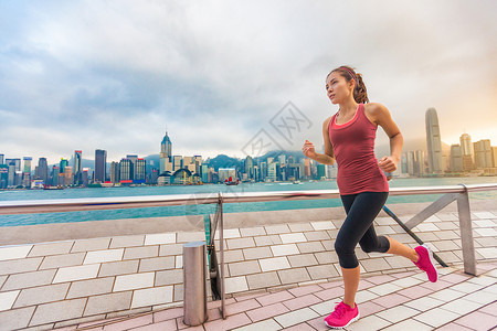 城市跑步-女子跑步者和香港天际线 女运动员健身运动员慢跑训练在九龙尖沙咀海滨长廊和星光大道上过着健康的生活方式背景图片