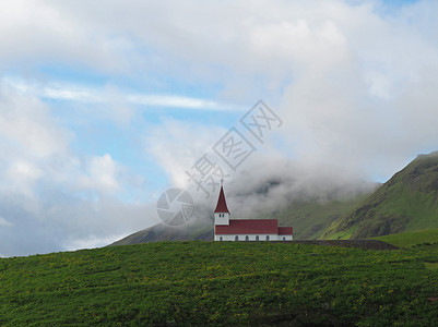 孤单的红白色教堂 在冰地绿草山和低云中背景图片