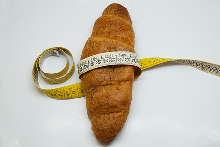 围绕羊角面包的软测量标尺 作为不健康营养的象征食物肥胖软尺工作室包子脆皮金子减肥生活方式烘烤背景图片