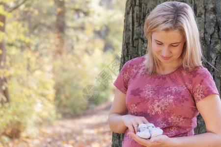 年轻孕妇在户外看编织婴儿靴子时生育力高清图片素材