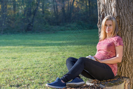 年轻孕妇的肖像正靠在树上坐着健康高清图片素材