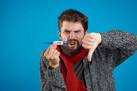 男人在蓝底健康药物和温暖衣物上吃药丸维生素发烧感染鼻子疾病药片疼痛药品围巾组织背景图片