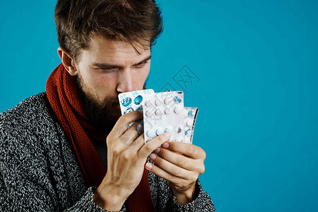 男人在蓝底健康药物和温暖衣物上吃药丸维生素流感药品蓝色围巾药片疾病鼻子发烧胶囊背景图片