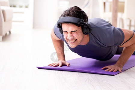 做个音乐素材男人在家里做运动和听音乐耳机举重二头肌肌肉娱乐训练躯干俯卧撑享受有氧运动背景