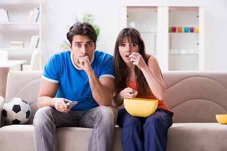 年轻男人在家和妻子一起看橄榄球女士电视幸福喜悦娱乐享受支持者闲暇情感爆米花游戏高清图片素材