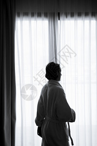窗前有浴袍的女人的休眠钟白色优雅窗帘睡衣女性窗户阳光酒店浴衣健康背景图片