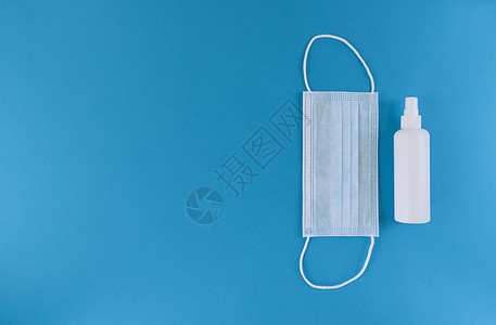 白色喷雾白色医疗面具和洗手液装在一瓶瓶子里 蓝色背景右侧有喷雾帽 简单平板上铺有复制空间 医学概念 库存照片背景