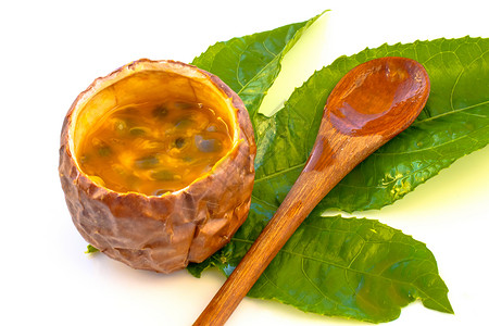 Maracuja在小玻璃容器里用木勺和白底的叶子将水果切成半截整片 果实黄色 果汁和种子甜点食物勺子异国木头玻璃茶匙饮食热带宏观背景图片
