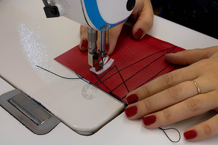 缝纫工具女裁缝在缝纫机上用红布缝制衣服 带活套和压脚特写的钢针工具工艺工厂剪裁材料作坊下水道纺织品行动裙子背景