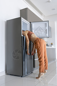 在炎热的一天 女孩在冰箱里用头凉快 空气调节器坏了冷却温度寒意体温厨房预报出汗广告气候技术背景图片
