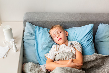 高发和头痛的生病小男孩躺在床上 拿着温度计 在科罗纳病毒流行时留在家中发烧孩子医院沙发疾病病人疼痛保健毯子温度鼻子高清图片素材