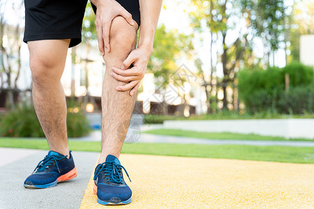 男性运动员腿部受伤和疼痛 手在公园里跑时抓着痛苦的膝盖按摩女性疾病女士十字形治疗抽搐事故赛跑者小牛背景图片