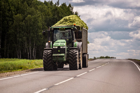 干草草机俄罗斯图拉 — 2019 年 7 月 30 日 在夏季道路上滚动的拖车中装有绿色青贮饲料的拖拉机背景
