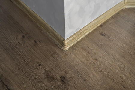 与具有木质纹理的塑料底板层压 家里新安装的强化木地板和踢脚板 现代设计 深色橡木地板镶木地板上塑料底座的特写风格角落控制板建筑学背景图片
