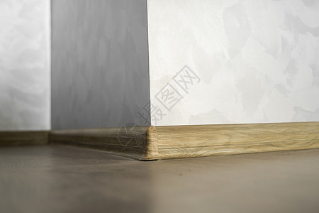 木头底座与具有木质纹理的塑料底板层压 家里新安装的强化木地板和踢脚板 现代设计 深色橡木地板镶木地板上塑料底座的特写角落房间住宅压板房子背景