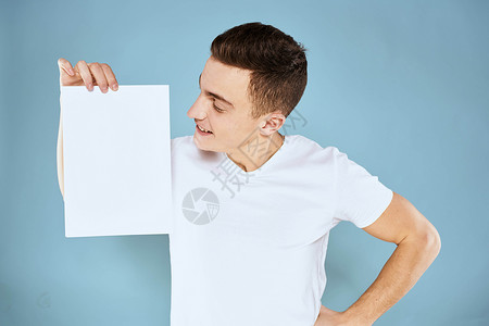 一个穿白色 T 恤的男人手里拿着一张纸 情绪是蓝色背景的裁剪视图 Copy Space推介会成功横幅卡片商业标语工作室商务男性人背景图片