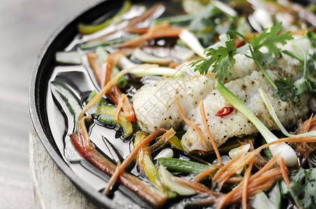 中国风格的中国式蒸鱼片 热盘上加蔬菜推介会热板鱼片美食电炉草药香料白色食物背景图片
