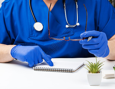 穿蓝色制服的男医生坐在白桌子上 写在纸笔记本上蓝色的高清图片素材