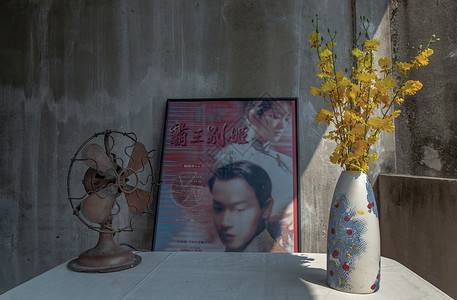 热情海报手工陶瓷花瓶中的黄色花朵和白色纹理桌布上的旧复古棕色金属风扇 带有中国古典海报电影框架和旧遗址水泥墙背景
