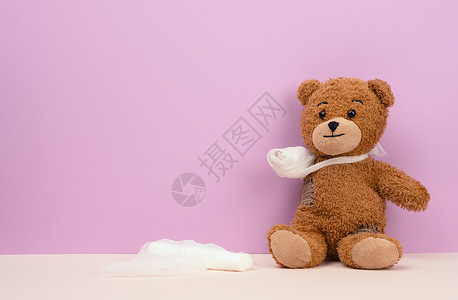长得风趣的棕褐色卷发泰迪熊 双脚掌和白纱布绷带 在紫色背景上背景图片