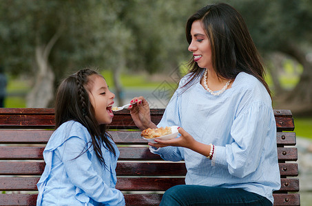 母亲和女儿坐在公园的长凳上 在公园里坐着女孩妈妈孩子闲暇成人女士父母童年街道乐趣可爱的高清图片素材