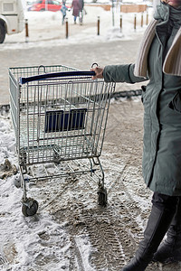 妇女在超市入口门前持有金属购物小卖车的妇女背景图片