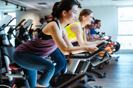 亚裔女人和朋友在健身房的健身自行车上纺纱体操女士乐趣运动朋友们训练团体男人中心背景图片