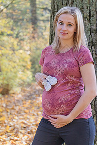 年轻孕妇展示婴儿靴子的年青孕妇肚子高清图片素材