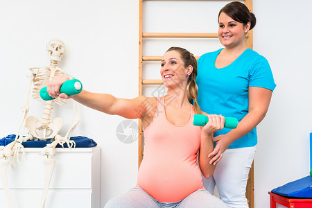 孕妇在物理治疗中与哑铃一起工作的怀孕妇女培训师私人自由重量器材疗法教练腹部助产士中心医生背景图片