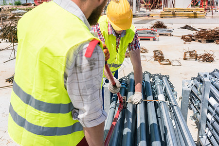 两名效率高的蓝领雇员在建造金属脚手架安全帽男性起重机耐用性合作团队建设同事就业建筑背景