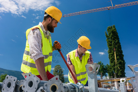 两名效率高的蓝领雇员建造一个金属脚手架员工背心建筑工作职业同事建设团队劳动者耐用性背景