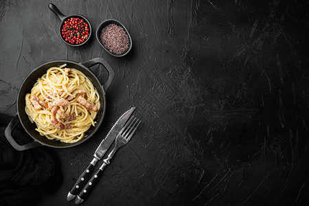 面食广告意大利面条 Carbonara 的菜肴 现代意大利面食配 guanciale 鸡蛋广告奶酪 铸铁煎锅 黑色石头背景 顶视图平躺背景