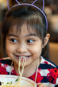 吃面条的亚洲女童 孩子吃拉面微笑着享受食物 孩子吃意大利面女孩勺子家庭美食午餐营养头巾筷子杯子酱高清图片素材