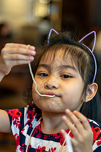 吃面条的亚洲女童 孩子吃拉面微笑着享受食物 孩子吃意大利面头巾勺子杯子家庭营养女孩午餐筷子美食好吃高清图片素材