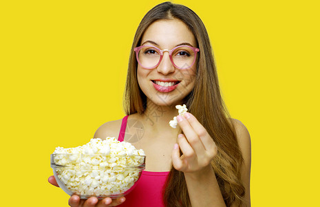 年轻美女拿着爆米花碗惊奇情感观众享受女性学生流行音乐快乐食物玉米背景图片
