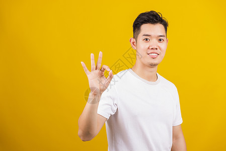 亚洲英俊的青年男子笑着正面握住 OK标志 用手和手指穿刺快乐微笑工作室手势学生黄色成人衣服胡须毛衣聪明的高清图片素材
