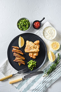 英国传统鱼和薯片 上面有薄荷豆泥和一片柠檬 黑圆板上印着白边和石头表面的顶视角熟的高清图片素材