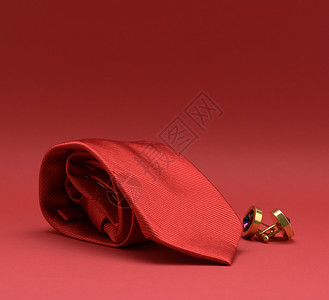 扭曲的丝绸红领带和红色背景的袖扣背景图片