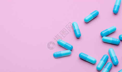 蓝色抗生素胶囊药丸散布在粉红色的背景上 抗生素耐药性 医药行业 医疗保健和医学概念 健康预算概念 胶囊制造业背景图片