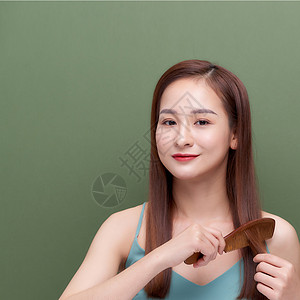 韩国造型素材穿着绿色背景梳理头发的可爱年轻女人的肖像快乐女孩女士梳子造型微笑刷子女性成人背景