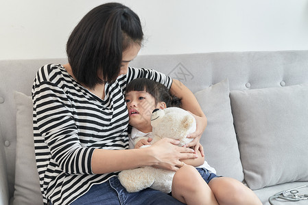 亚裔母亲接受小学龄前受挫的孩子坐在家里的沙发上美丽的高清图片素材