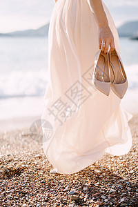 手握着高胸鞋的新娘在海滩上走来走去背景图片