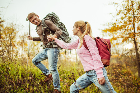男人牵着女人的手帮助女人爬山 另一只手拿着登山杖 徒步旅行的概念 支持和协助概念休闲背包微笑生活方式冒险家庭幸福阳光乐趣友谊女朋友高清图片素材