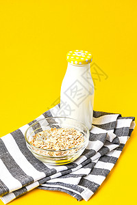 碗里吃燕麦 玻璃瓶里装牛奶 用鲜黄色的浅黄色背景和厨房毛巾 复制空间背景图片