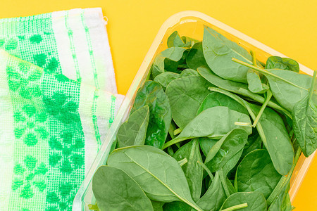 黄色背景透明塑料套件中新鲜的婴儿菠菜叶新片草本植物饮食排毒沙拉树叶绿色食物生食植物活食背景图片