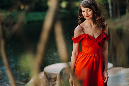 长着长发的长红裙子笑着女孩在树林中公园散步时身穿长红色礼服日落成人森林公主自由裙子摄影派对魔法奢华背景图片
